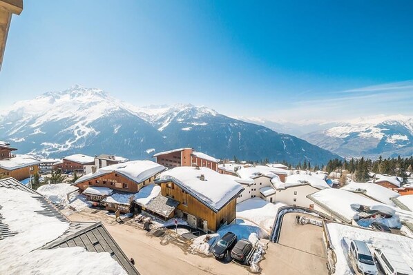 A snow-covered mountain village with wooden buildings and a clear view of snow-capped mountains in the background.