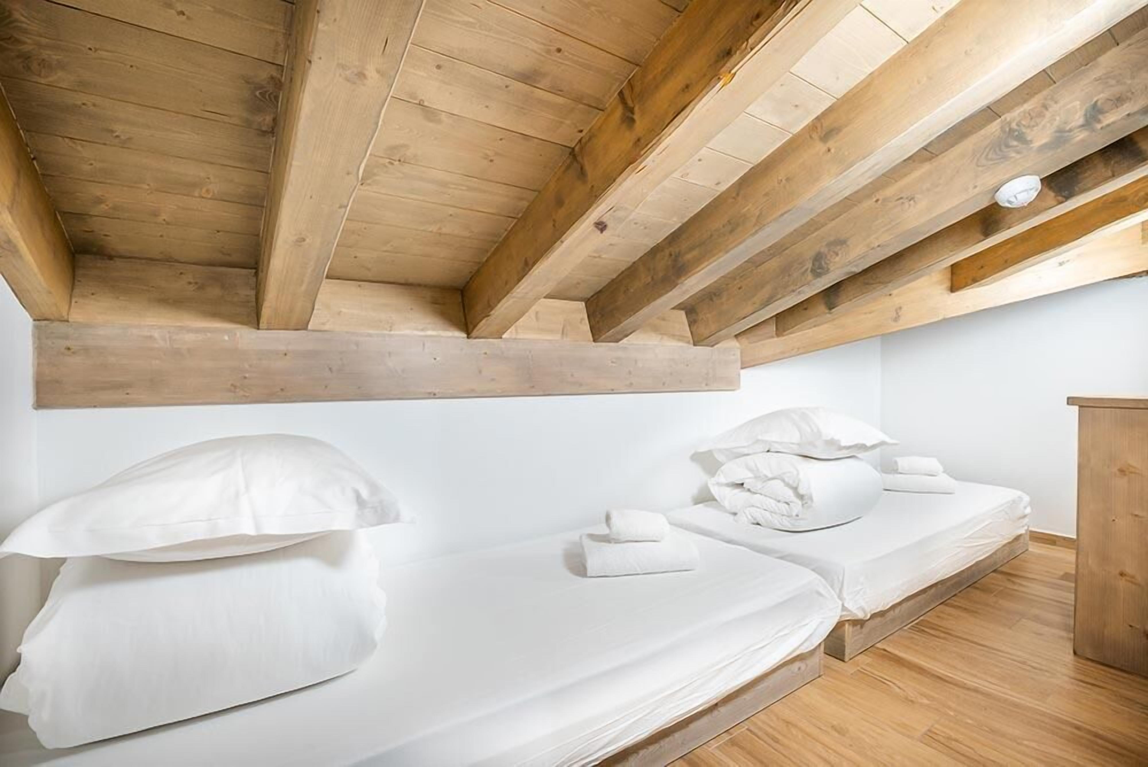 Een slaapkamer met een houten plafond, een bed met witte lakens en een houten vloer.