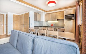 Een kleine keuken met houten kastjes, een magnetron, en een eethoek met een tafel en stoelen.