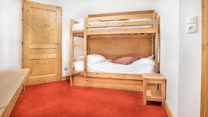 A bunk bed with a wooden frame, a red carpet floor, and a wooden door.