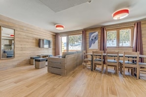 Een moderne woonkamer met houten wanden, een bank, een televisie en een eethoek met stoelen en een tafel.