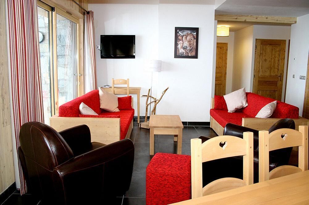 A room with a red sofa set, wooden chairs, a small table, and a TV mounted on the wall.