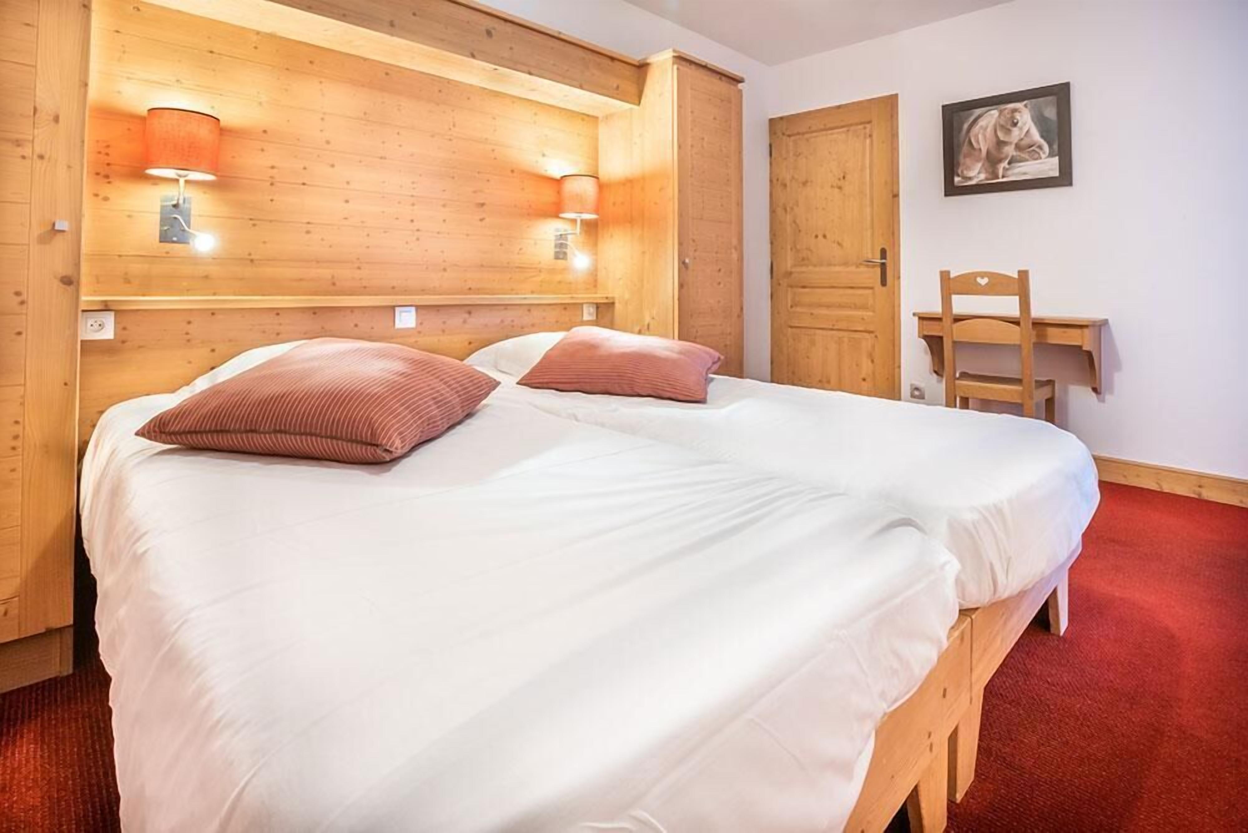 Ein Zimmer mit Holzboden, einem Bett, zwei Wandlampen, einem Schreibtisch und einem Stuhl.