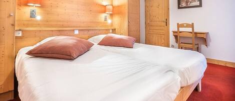 A wooden room with a bed, two wall-mounted lamps, a desk, and a chair.