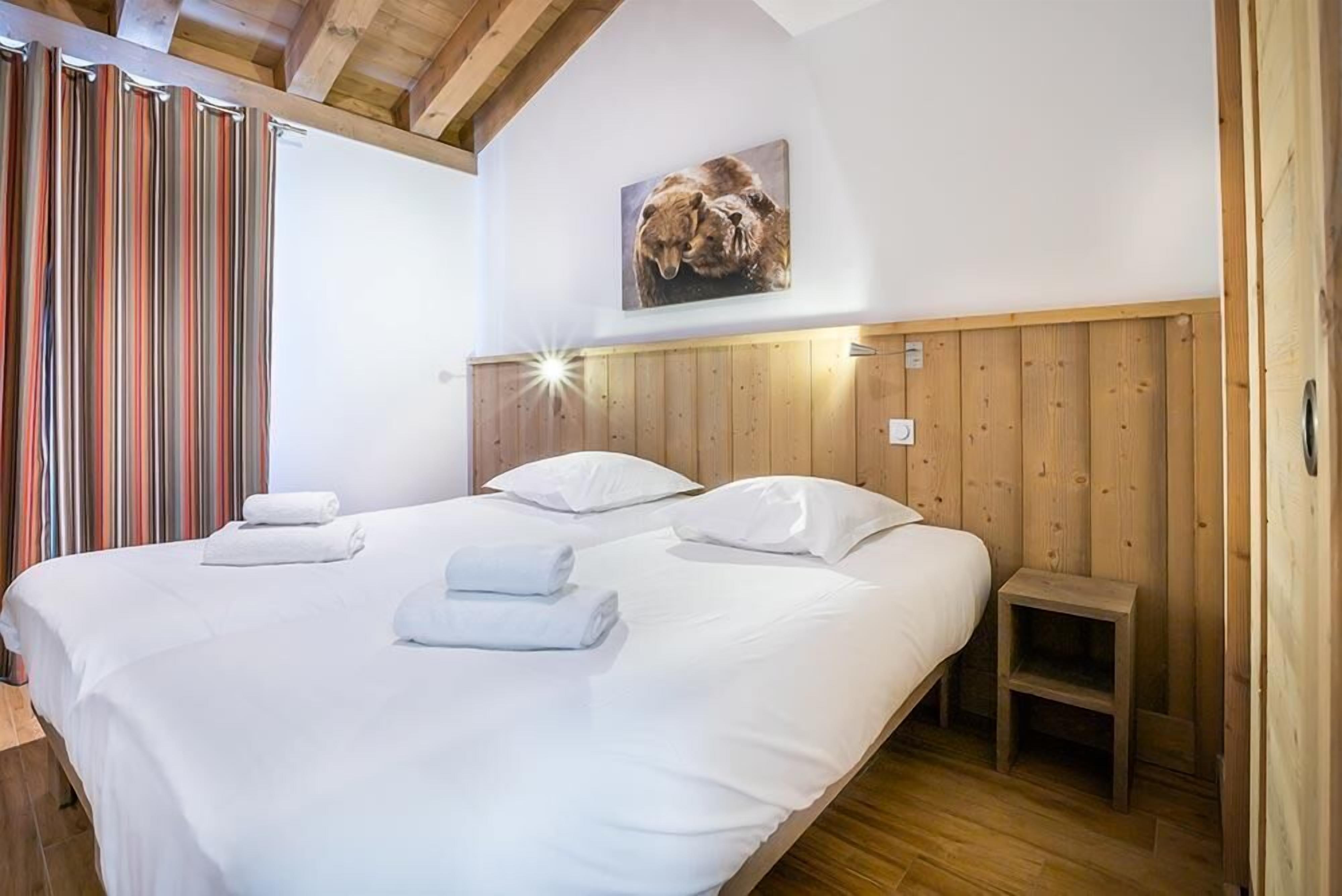 A double bed with white linens and pillows, a wooden headboard, a small wooden nightstand, and a wall-mounted light fixture.