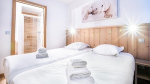 A hotel room with two beds, wooden headboard, white linens, a polar bear artwork, and a wooden door.