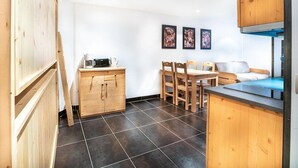 Una cocina compacta con armarios de madera, una mesa de comedor y sillas. Hay dos cuadros en la pared.