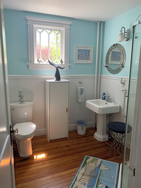 A bathroom with a toilet, a pedestal sink, a window with a whale tail decoration, a small rug, and a shower with a glass door. - Beautifully home in Newport RI. Five star ratings in all previous rentals. (Newport)