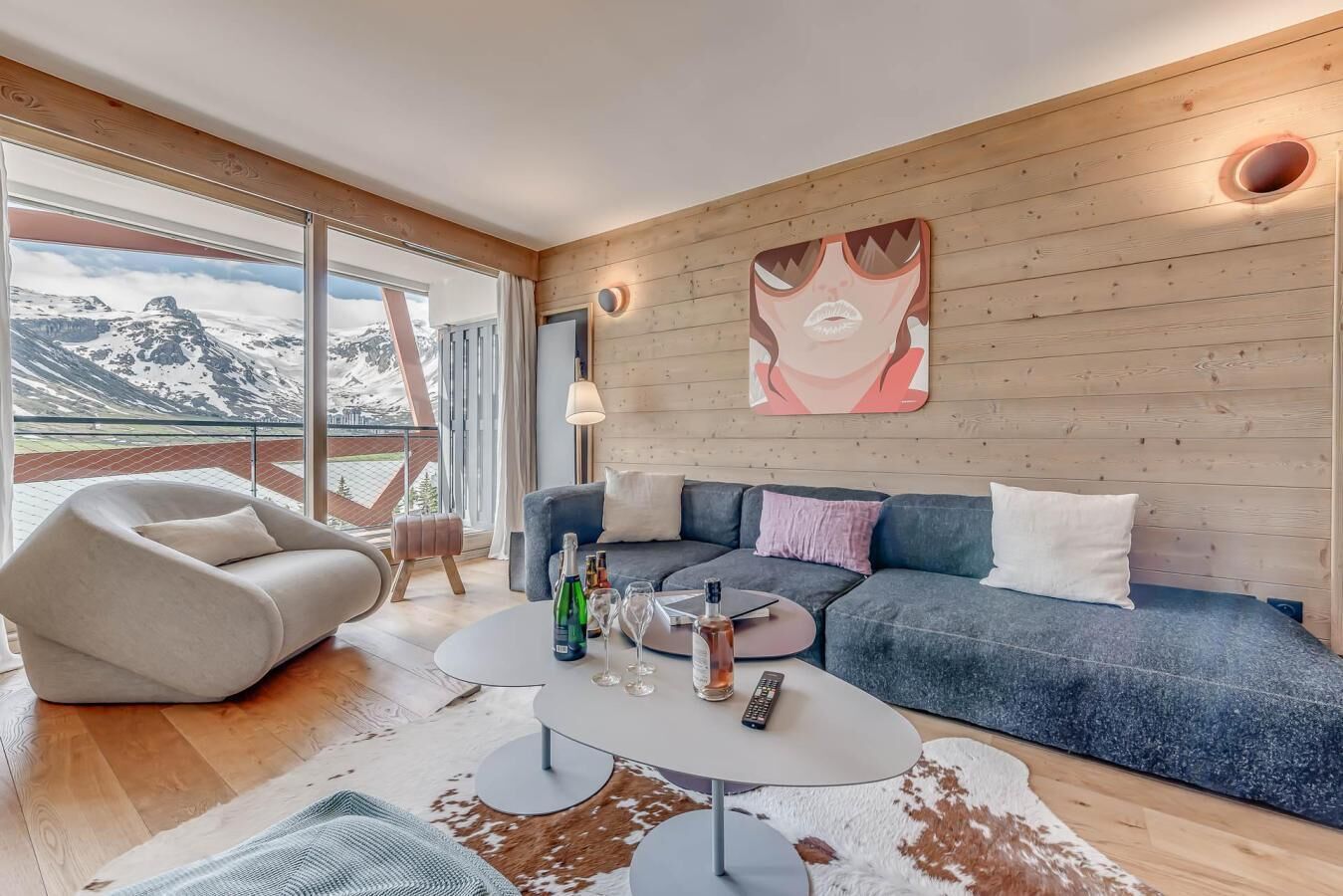 A modern living room with a sofa, armchair, and a dining table with bottles and glasses.