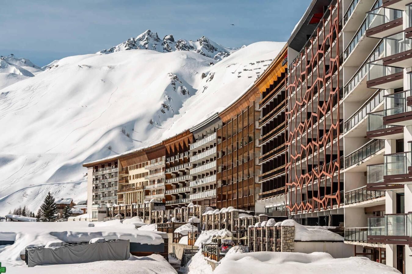 Un hotel con varios pisos, balcones y montañas al fondo.