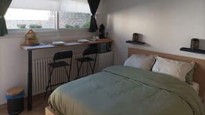 A bedroom with a bed, a desk with chairs, a radiator, a window with curtains, and a small shelf with decorative items. - " LE 16 BAIE DE SOMME, STUDIO D HOTE"
TERRASSE ET JARDIN  (Friville ESCARBOTIN)