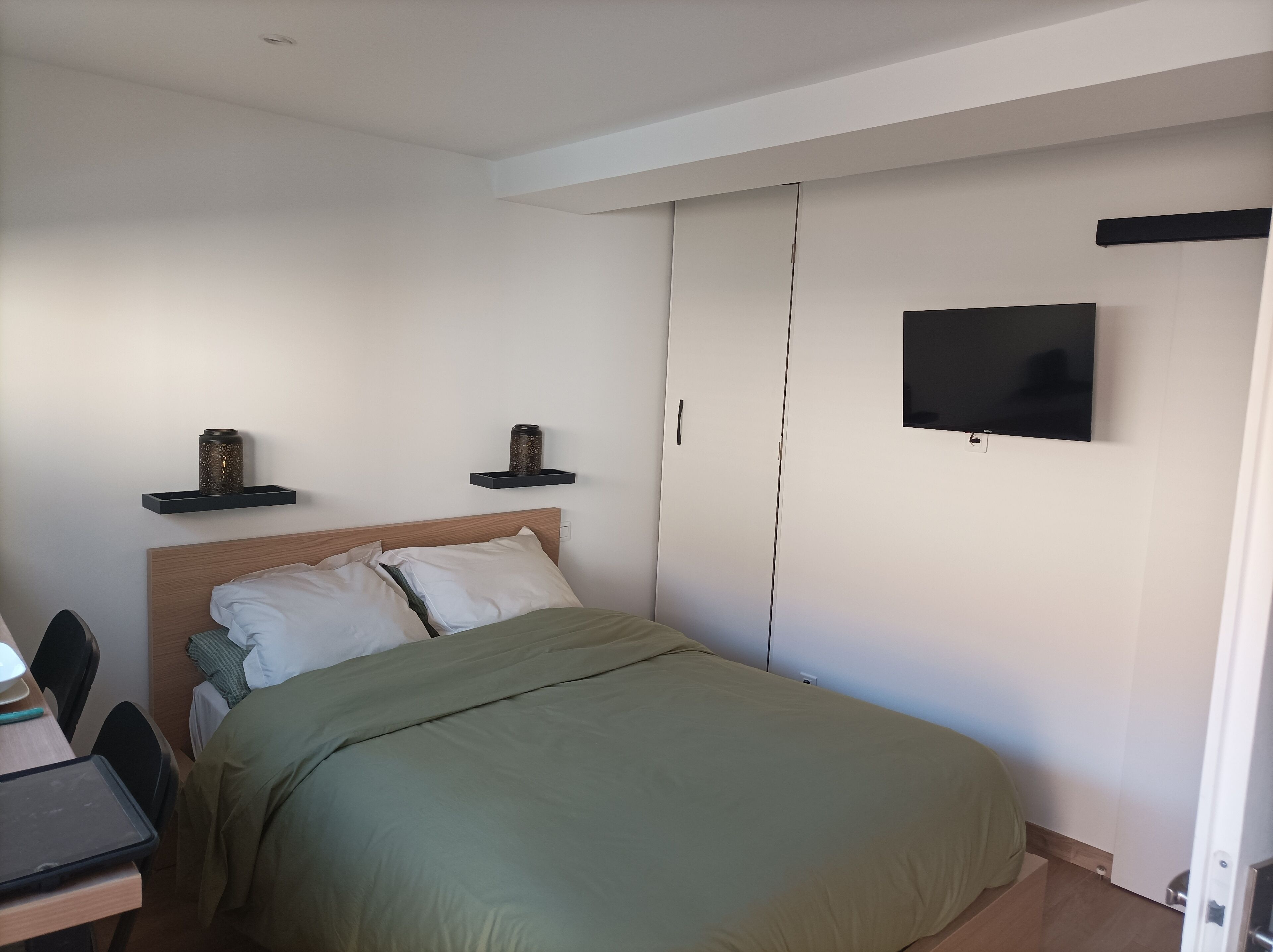 Un dormitorio con cama, escritorio con computadora portátil, televisor y armario.