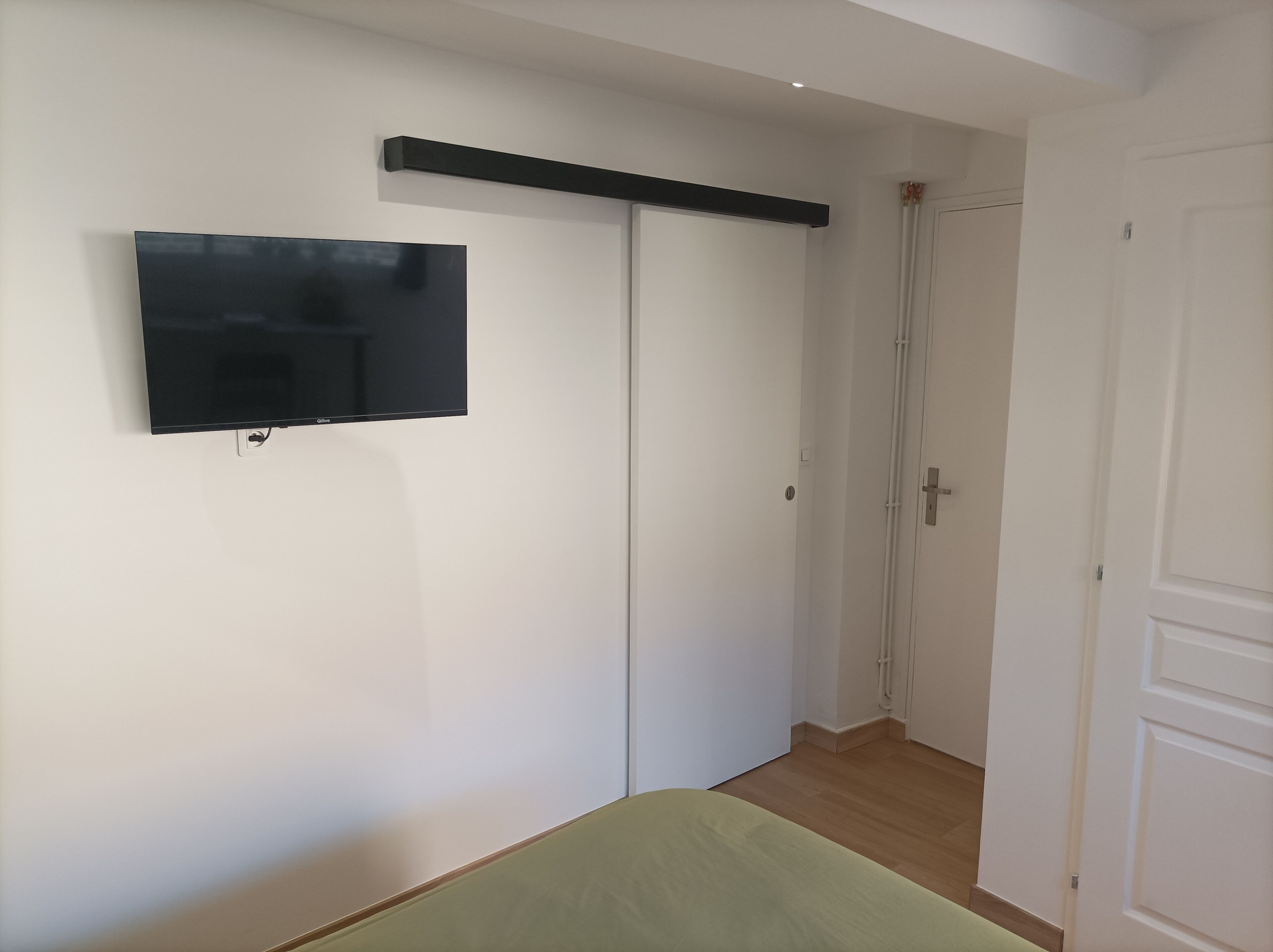 Un dormitori amb un llit, una televisió penjada a la paret i un armari.