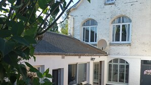 A two-story building with a white exterior, large windows, and a small attached structure with a tiled roof. - " LE 16 BAIE DE SOMME, STUDIO D HOTE"
TERRASSE ET JARDIN  (Friville ESCARBOTIN)