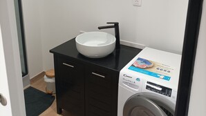 A compact bathroom with a black vanity, a white sink, and a front-loading washing machine. - " LE 16 BAIE DE SOMME, STUDIO D HOTE"
TERRASSE ET JARDIN  (Friville ESCARBOTIN)