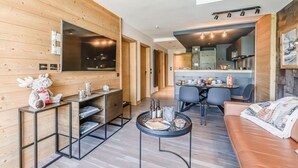 A modern living room with a wooden wall, a sofa, a coffee table, and a dining area with chairs and a table. - 200m from ski slopes, 4th floor, view lake, balcony, ski locker, 50m², Tignes (Tignes)