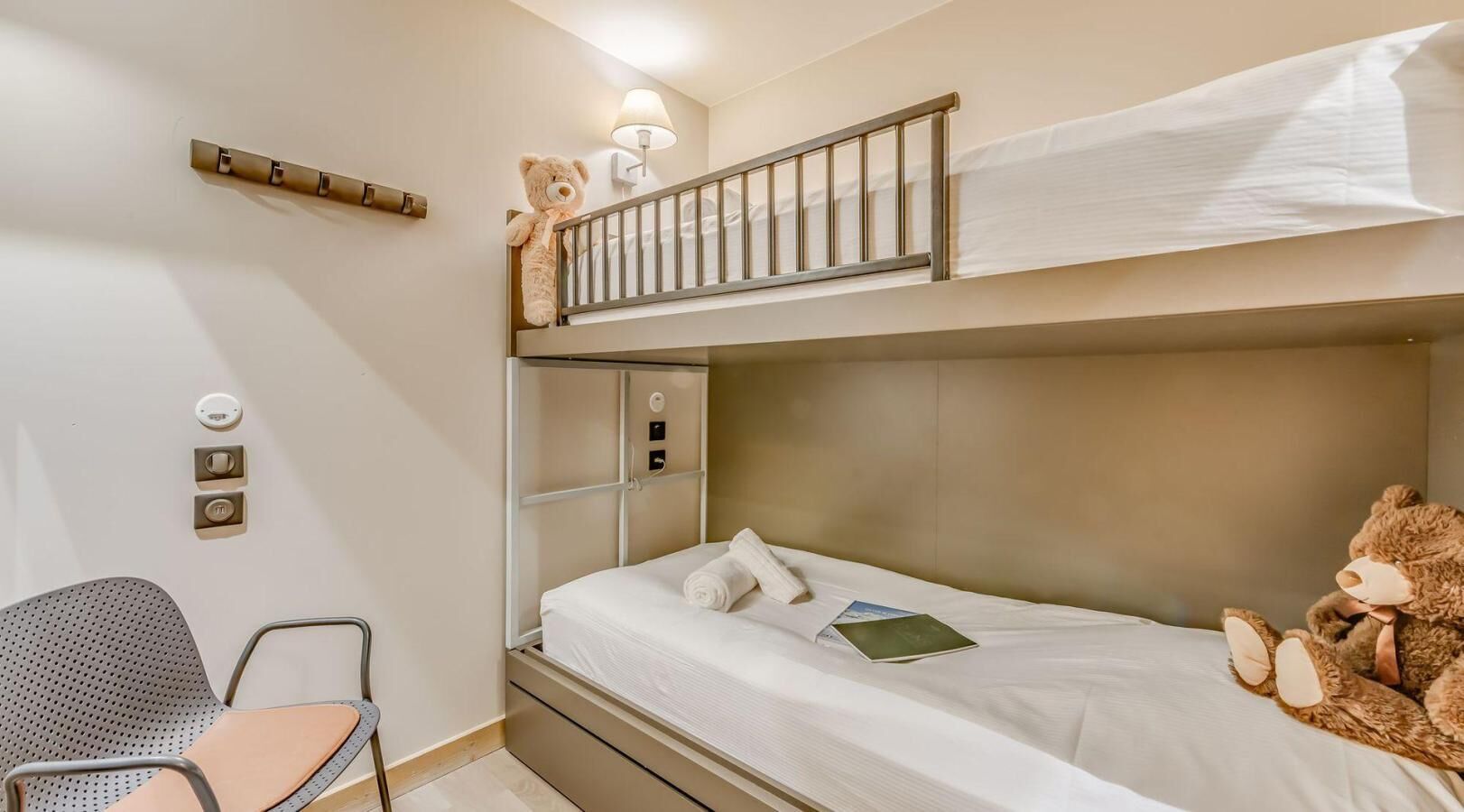 Une chambre avec un lit superposé, un bureau, une chaise et deux ours en peluche.