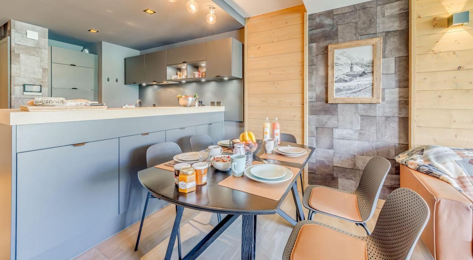 Een moderne keuken met een centraal eiland, een eethoek met een ronde tafel en stoelen, en een stenen accentmuur met een ingelijst kunstwerk.