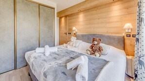 A hotel room with a large bed, wooden headboard, two bedside lamps, a teddy bear, and a nightstand with a lamp. - 200m from ski slopes, 4th floor, view lake, balcony, ski locker, 50m², Tignes (Tignes)
