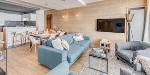 Una sala moderna con un sofá azul, un sofá gris y una mesa de centro. Hay una zona de comedor con una mesa y sillas.