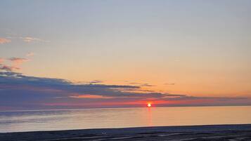 Una playa al atardecer con el sol bajo en el horizonte, mar tranquilo y cielo despejado.
