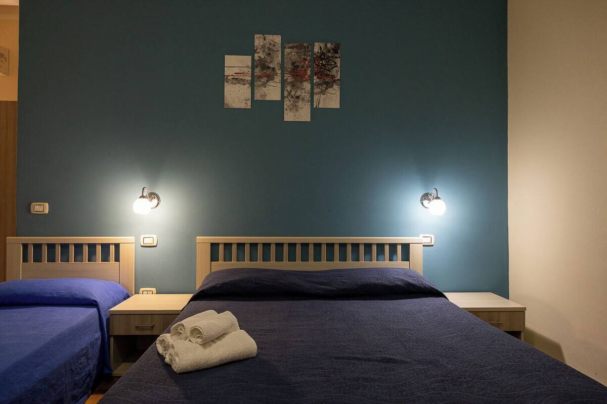 Ein Hotelzimmer mit zwei Betten, einem Nachttisch, einem Wandbild und einer Steckdose.