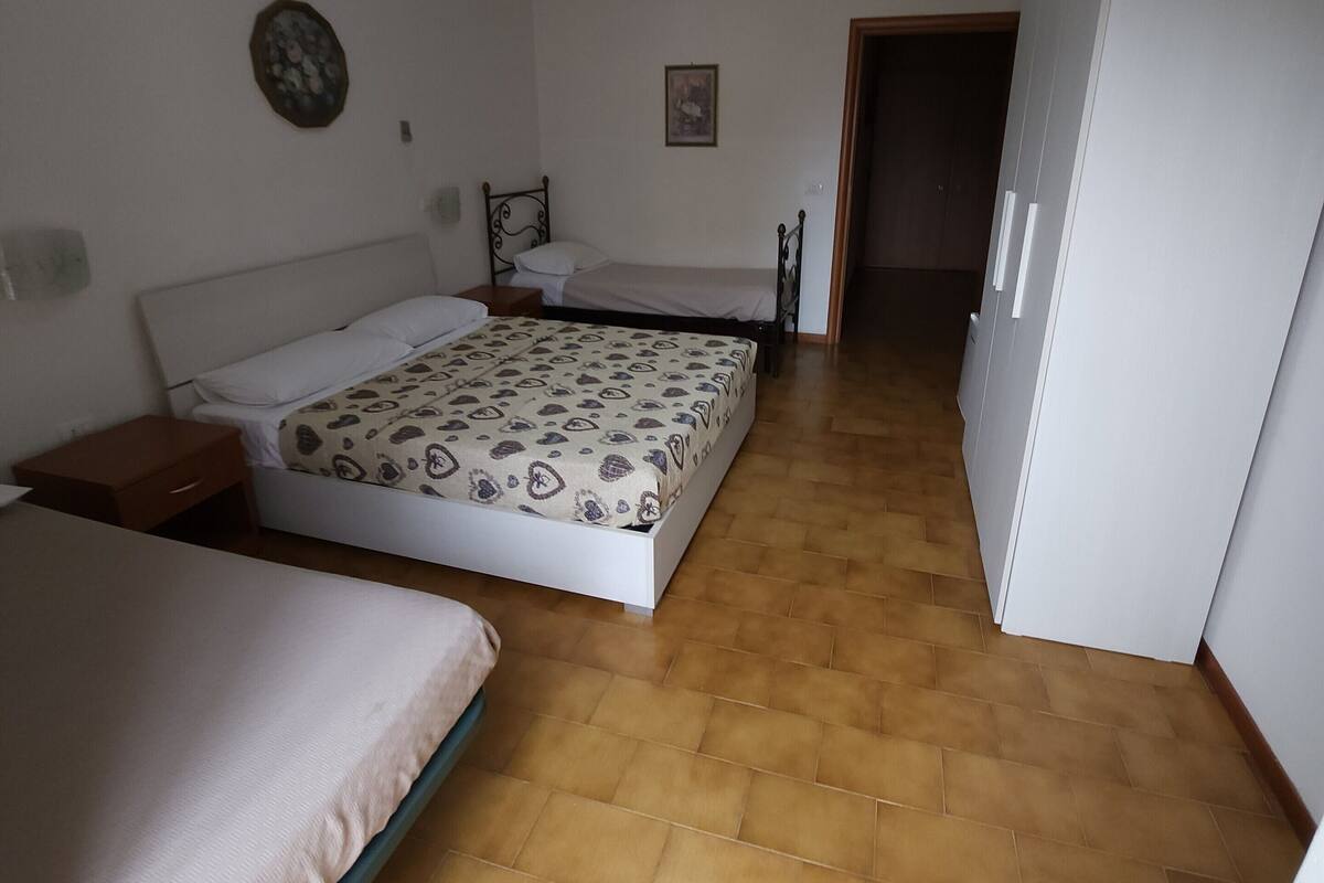 Ein Schlafzimmer mit zwei Betten, Holzboden, Deckenleuchte und einer Tür zu einem anderen Raum.