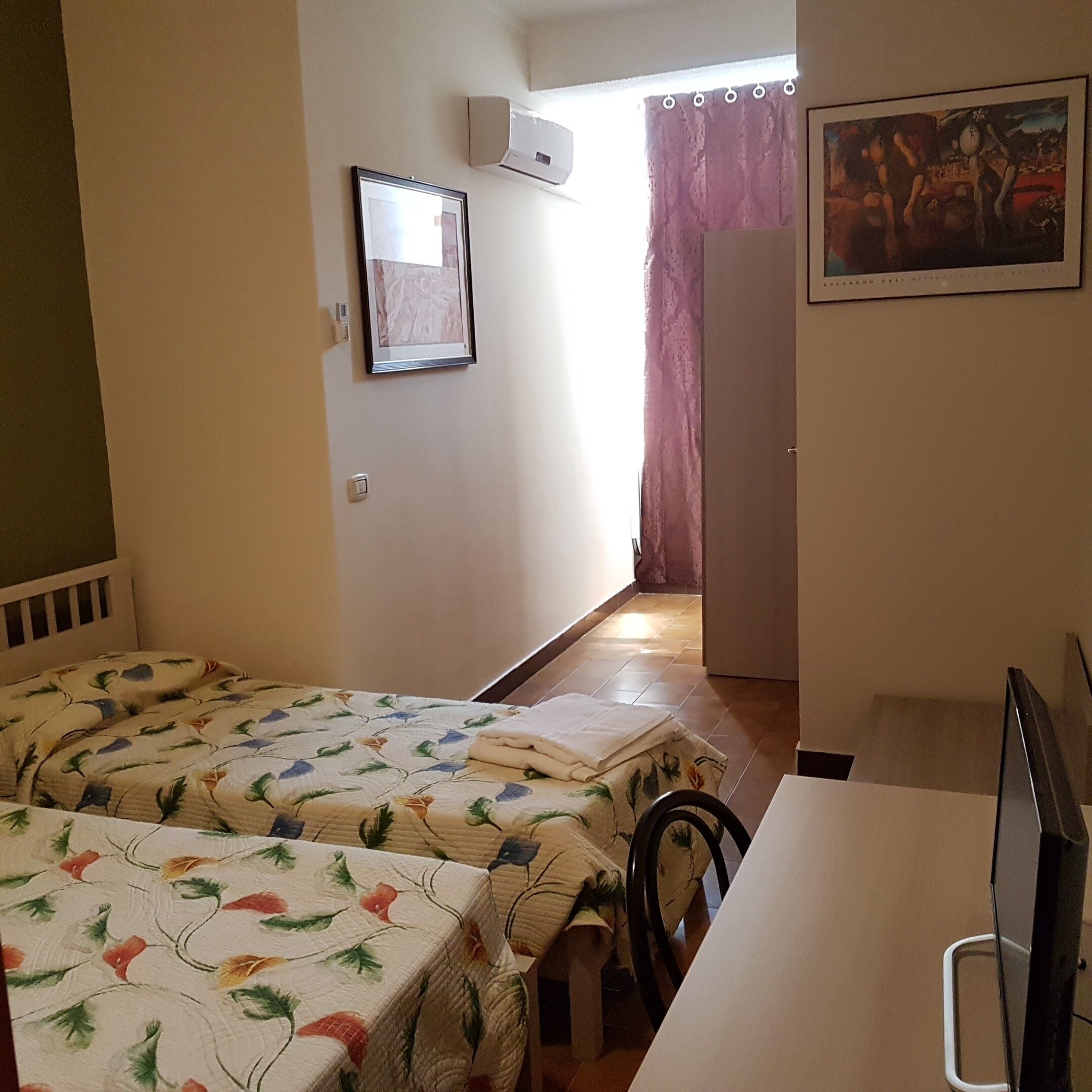 Ein Zimmer mit zwei Betten, einem Schreibtisch, einem Sessel, einem Fernseher und einem Bild an der Wand.