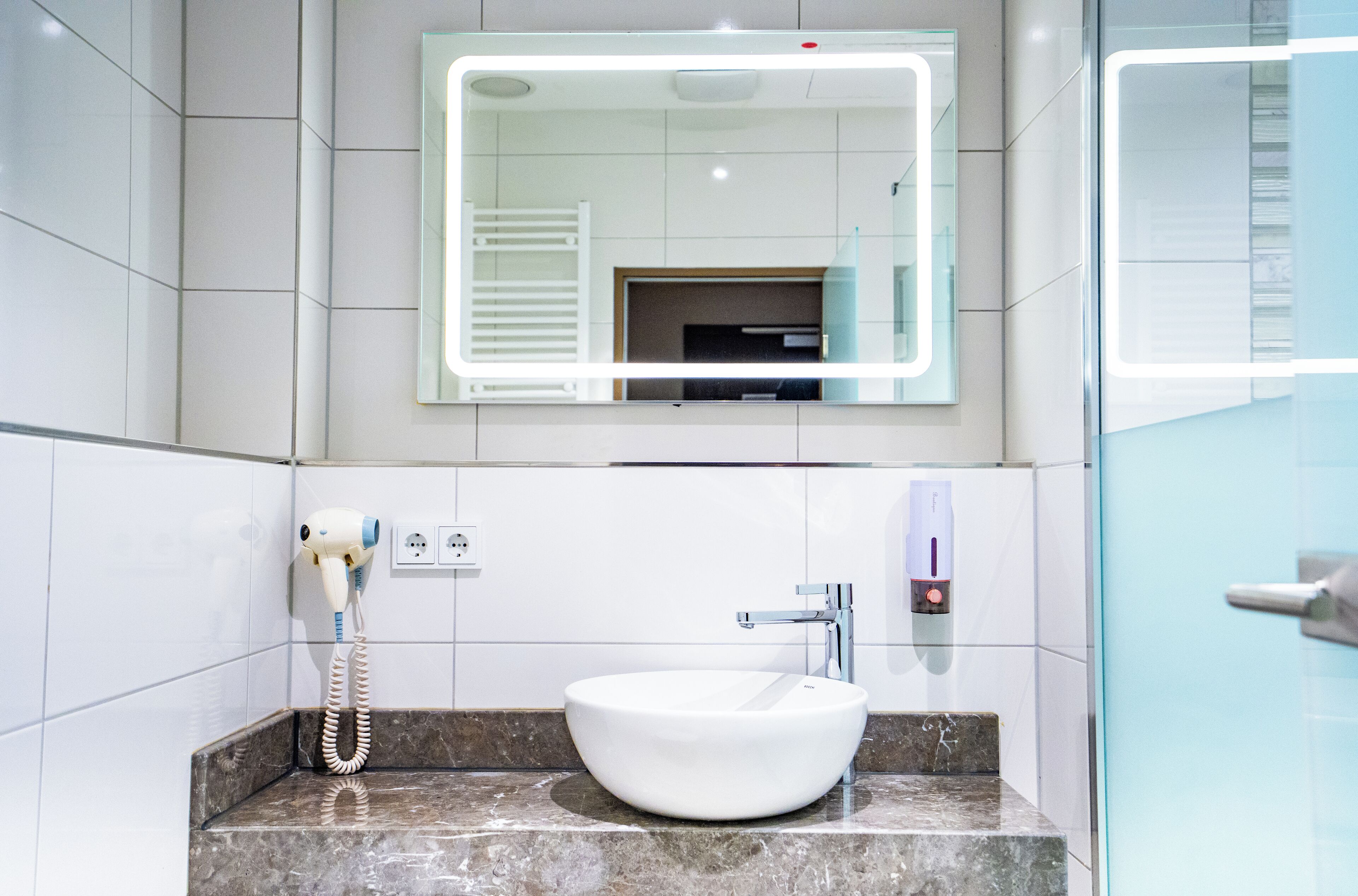 A bathroom with a white sink, a mirror, and a hairdryer on the wall.