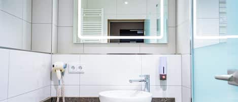 A bathroom with a white sink, a mirror, and a hairdryer on the wall.