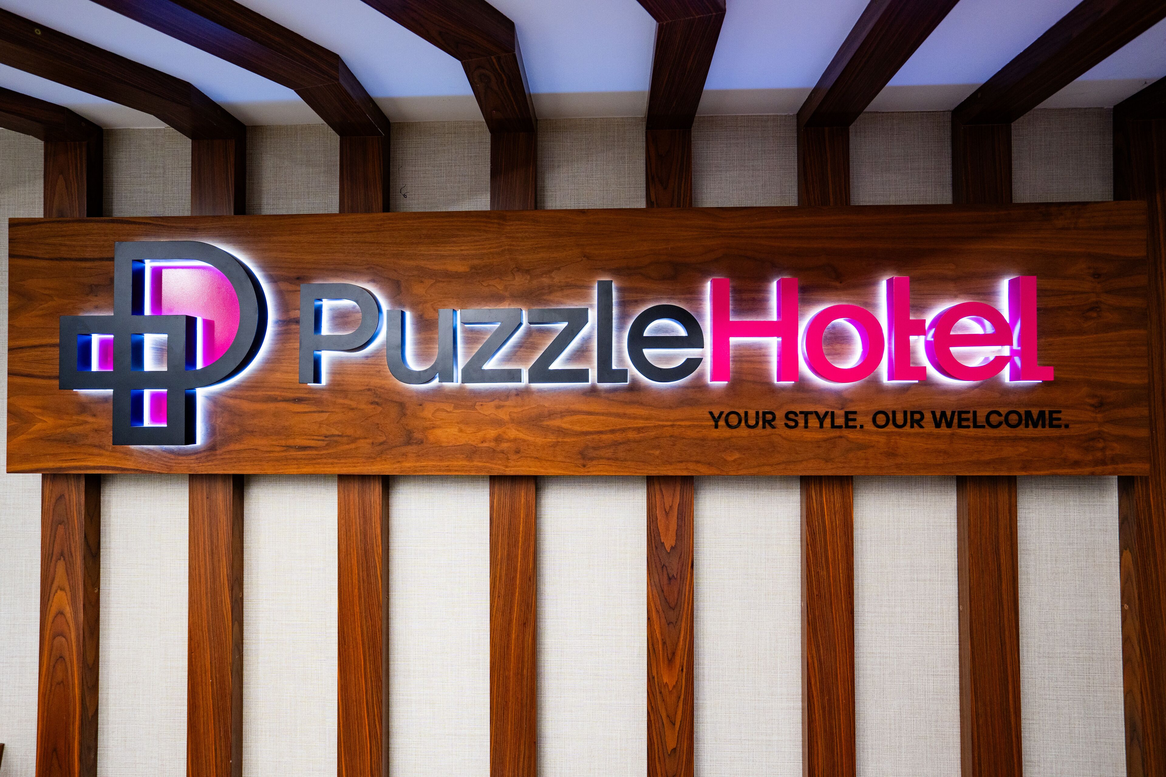 A wooden sign with the text 'Puzzle Hotel' and a logo, indicating the name of the establishment.