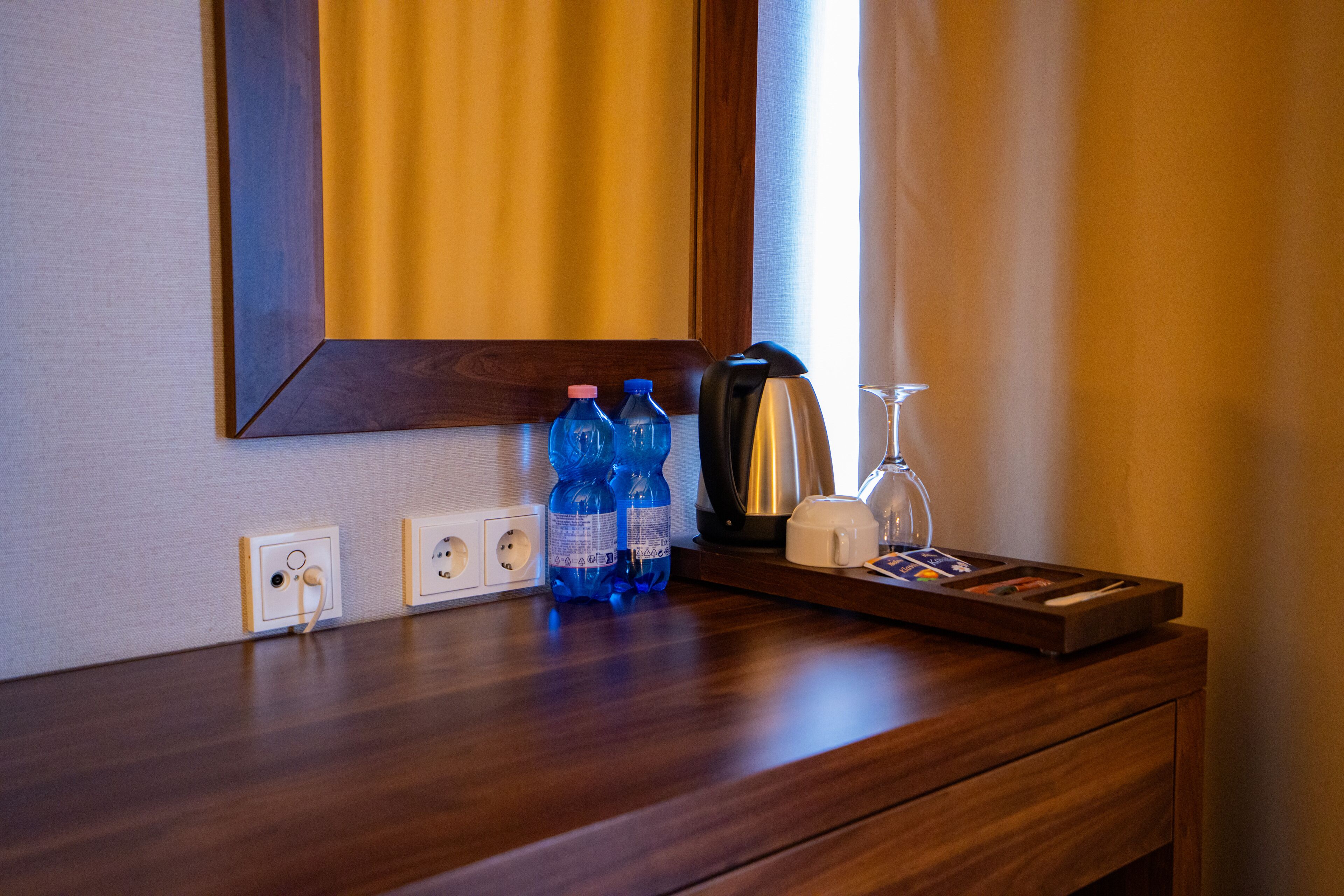 Un comptoir en bois avec un miroir, deux bouteilles d’eau, une machine à café, un verre et un plateau avec des cartes.