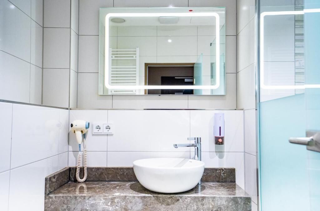 Un baño con lavamanos blanco, un espejo y un secador de pelo en la encimera.
