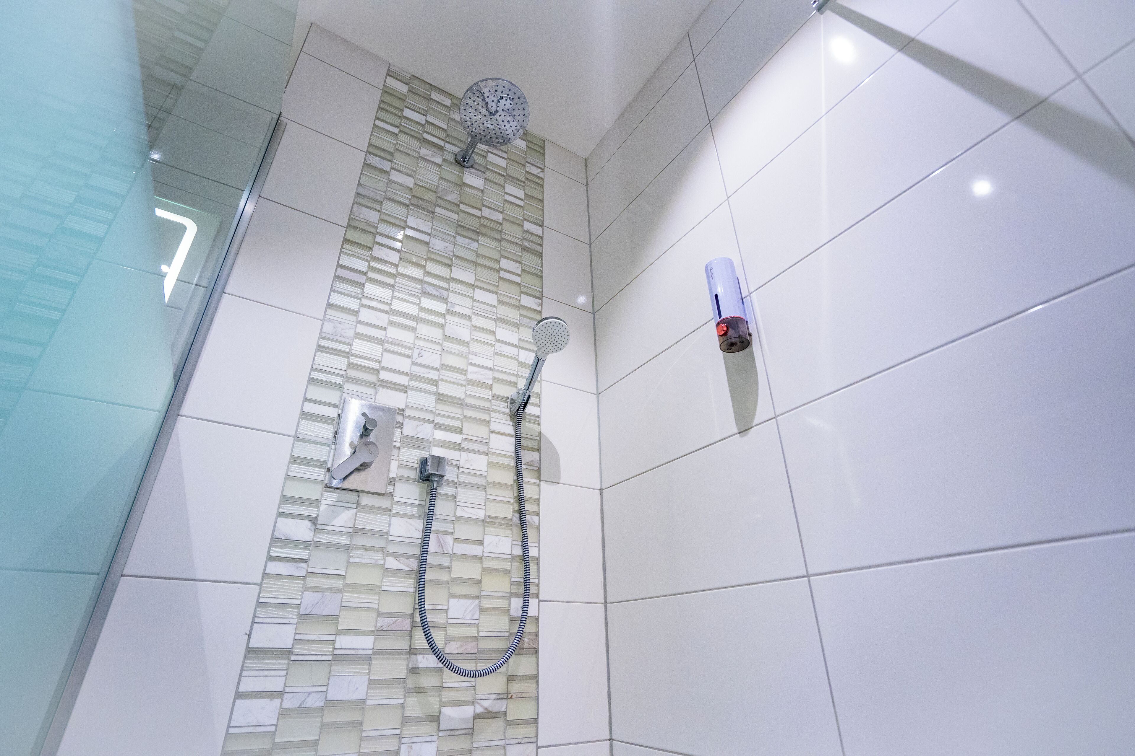 A modern bathroom with a glass shower enclosure, a handheld showerhead, and a wall-mounted faucet.