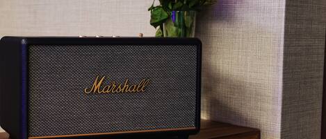 Un altavoz Marshall sobre una mesa de madera con un jarrón de flores rosas al fondo.