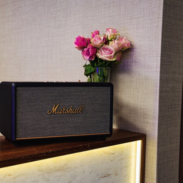 Un altavoz Marshall sobre una mesa de madera con un jarrón de flores rosas al fondo.