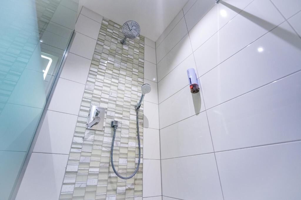 Une douche avec une porte en verre, une douchette à main et un robinet fixé au mur.