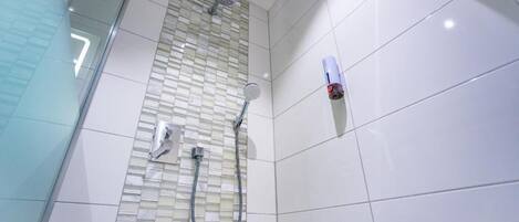 Une douche avec une porte en verre, une douchette à main et un robinet fixé au mur.