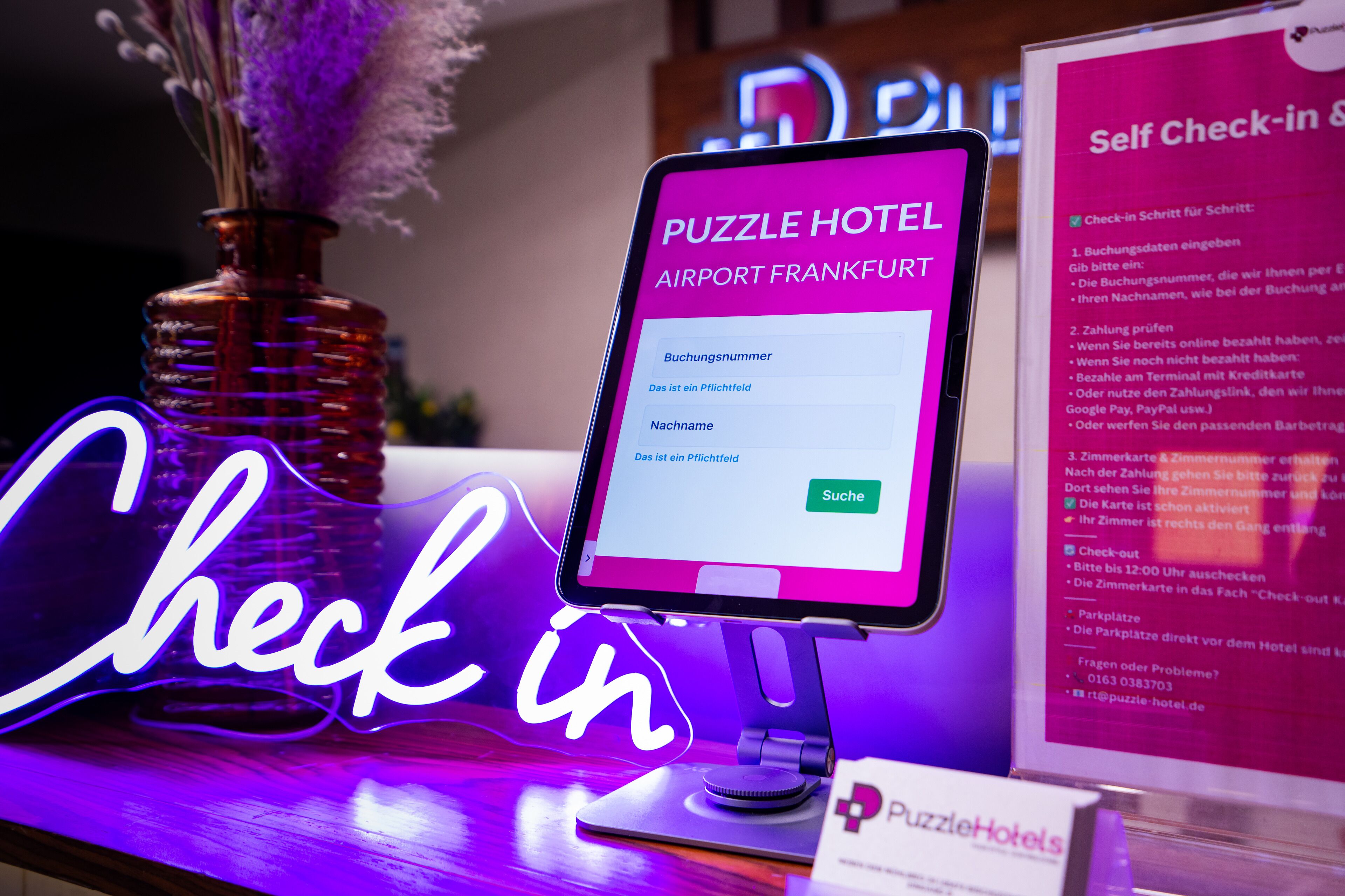 A self-check-in kiosk at Puzzle Hotel Airport Frankfurt with a neon sign.