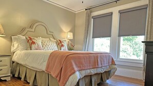 Un dormitorio con cama, mesitas de noche, lámpara y ventana con cortinas.