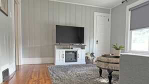 Una sala de estar con chimenea, televisor y un sofá gris.
