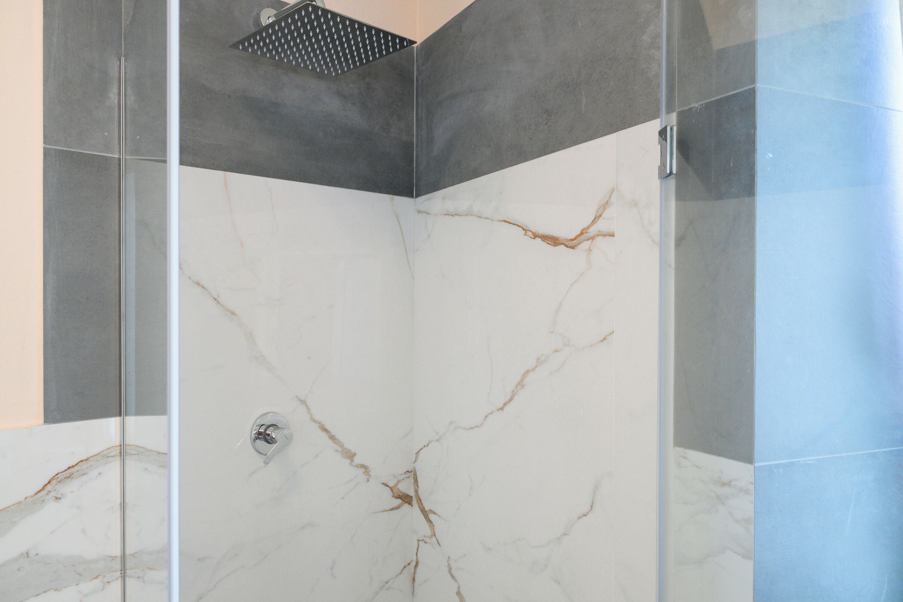 A shower with a glass door and marble walls.
