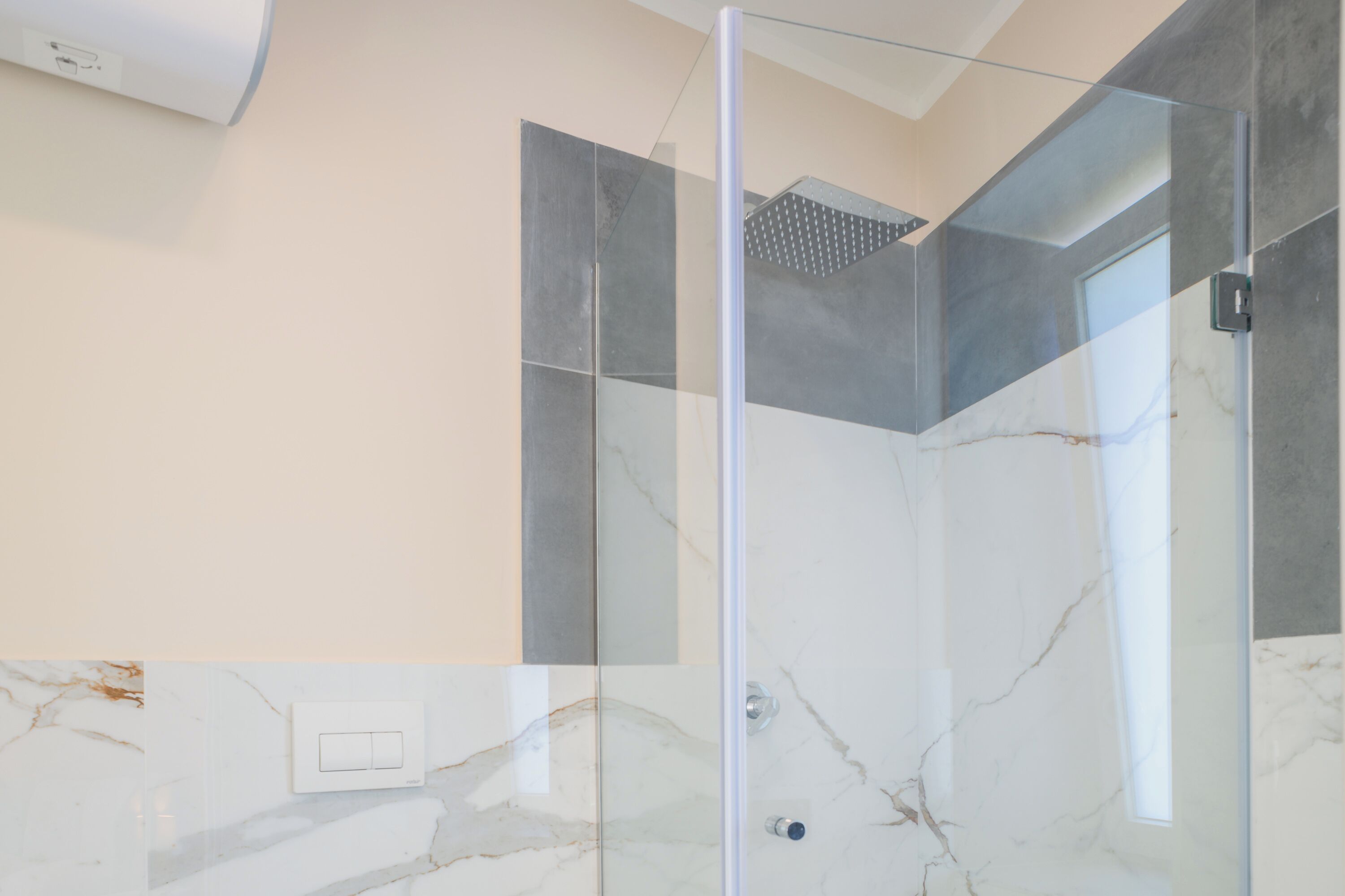 Une salle de bain moderne avec une douche à l’italienne en verre, des carreaux de marbre et un interrupteur visible.
