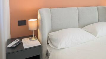 A neatly made bed with white linens, a bedside lamp, a remote control, and a notepad on a nightstand.