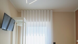 A modern bathroom with a flat-screen TV mounted on the wall, a white shower curtain, and a ceiling light fixture. - Aphrodite House (Pompei)