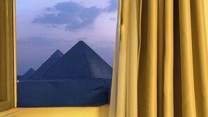 Una ventana con cortinas, mostrando vistas de pirámides bajo un cielo despejado.