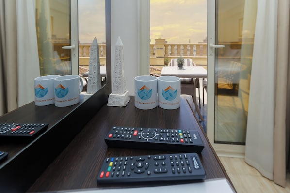 A table with two remote controls, three mugs, and a small pyramid model.
