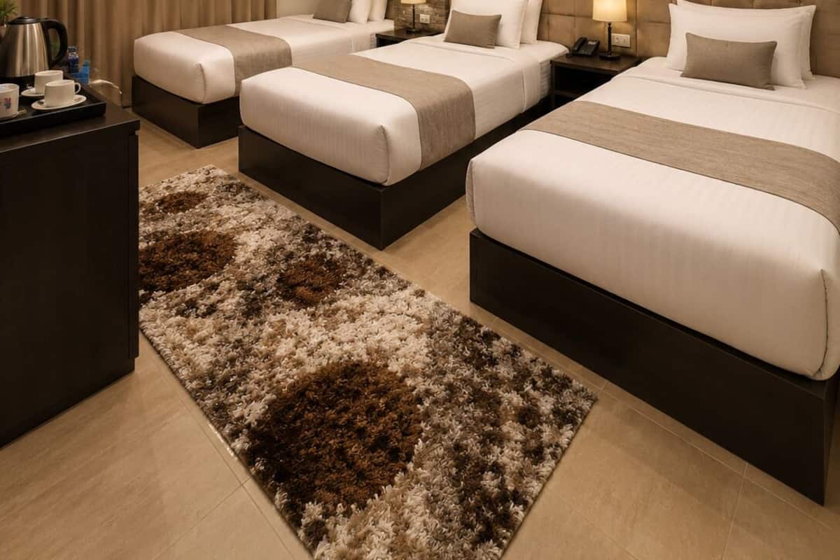 A hotel room with three beds, a large window, a stone accent wall, and a modern light fixture.