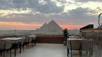 Una terraza en la azotea con mesas y sillas, vistas a pirámides y un cielo nublado.
