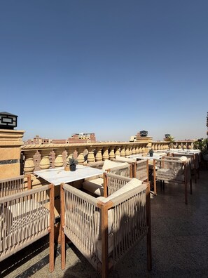 A rooftop terrace with multiple tables and wicker chairs, offering a view of the cityscape.